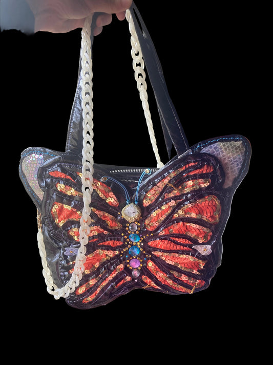 Decorative handbag with butterfly design and sequins held by a hand.